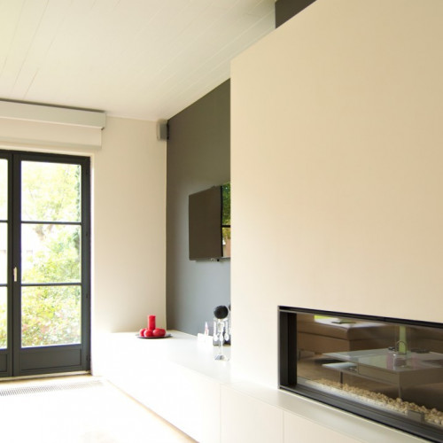 Bij dit project was de haardwand reeds geïnstalleerd.  De bewoners wouden rondom het haardmeubel nog een kastenwand. In de lage kast is plaats voorzien voor alle toestellen, rechts naast de haard loopt de kast over naar een dressoir die aansluit bij de eettafel. De kast is volledig naadloos gelakt in satijnlak. Kast-ID Asse